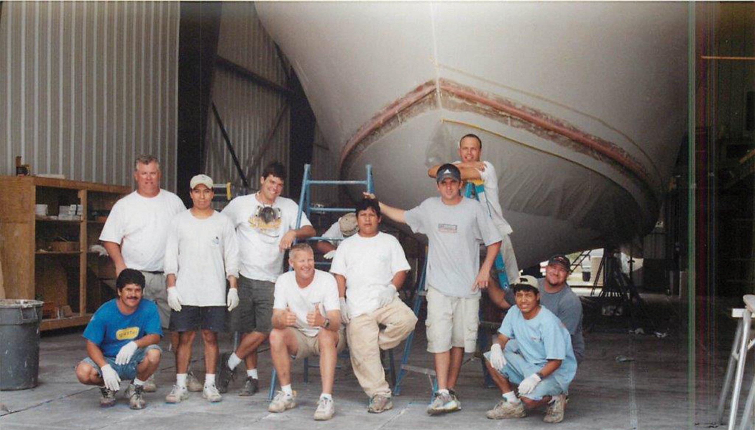 Bayliss Boatworks workers stopping work for a picture in front of a boat bow in a build shed
